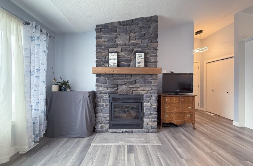 Unfurnished living room with wood-type flooring, a stone fireplace, and a textured ceiling