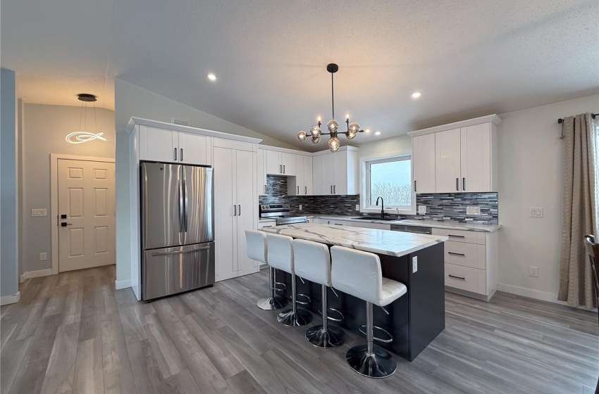 Kitchen with vaulted ceiling, appliances with stainless steel finishes, decorative light fixtures, white cabinetry, and a center island