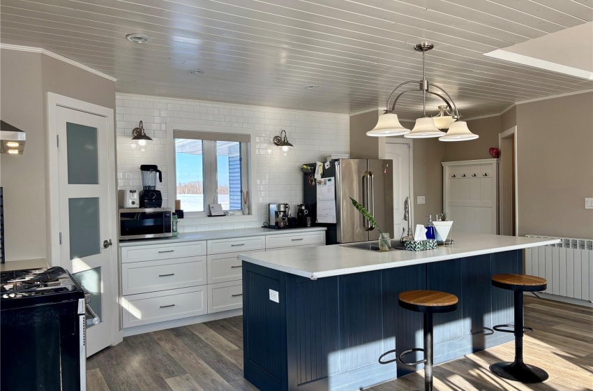 Kitchen featuring white cabinetry, decorative light fixtures, a center island, appliances with stainless steel finishes, and radiator heating unit