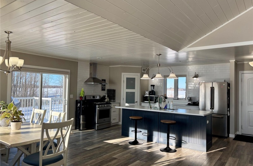 Kitchen featuring pendant lighting, appliances with stainless steel finishes, a kitchen island with sink, and wall chimney range hood