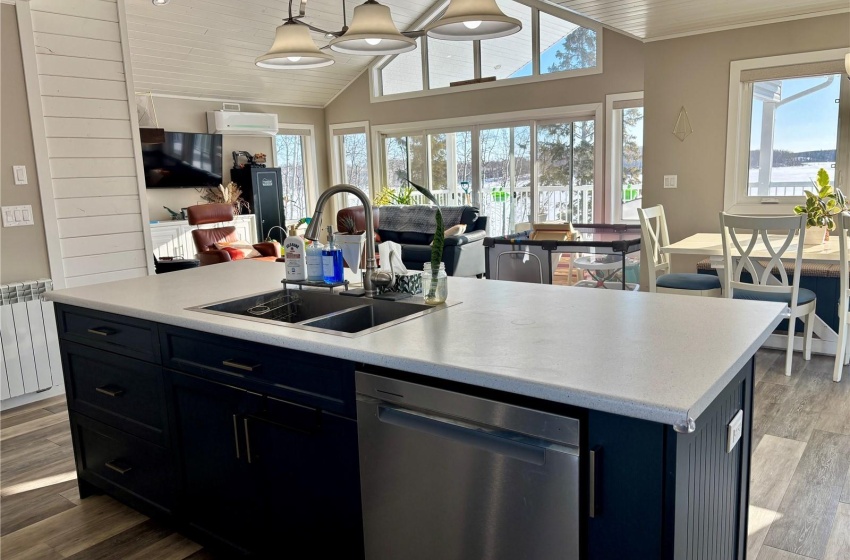 Kitchen featuring radiator, sink, hanging light fixtures, a kitchen island with sink, and stainless steel dishwasher