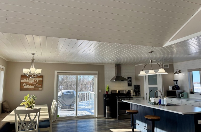 Kitchen featuring stainless steel appliances, an island with sink, hanging light fixtures, and wall chimney range hood