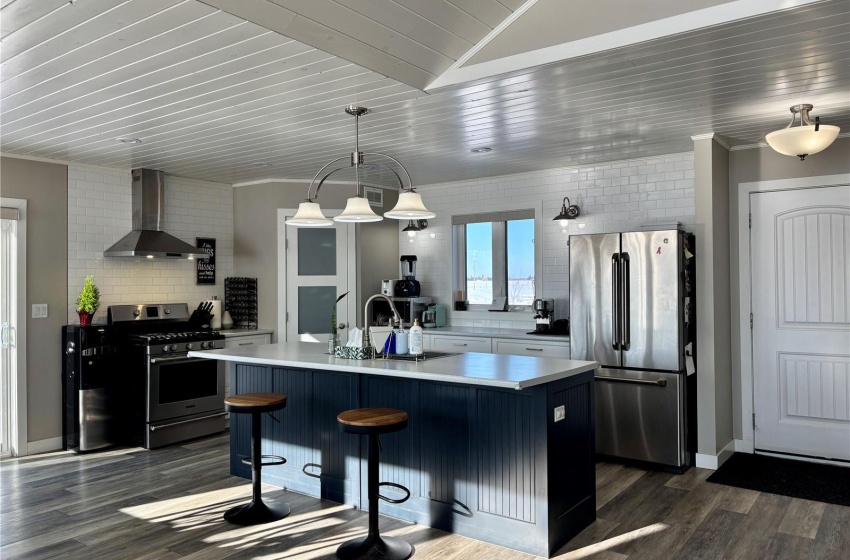 Kitchen featuring appliances with stainless steel finishes, a breakfast bar, pendant lighting, a kitchen island with sink, and wall chimney range hood