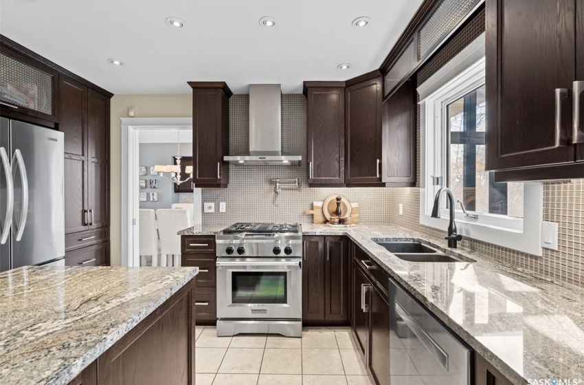 Kitchen with wall chimney exhaust hood, stainless steel appliances, sink, and light stone counters