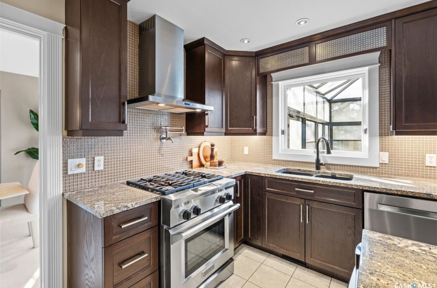 Kitchen featuring wall chimney range hood, light stone countertops, sink, and appliances with stainless steel finishes