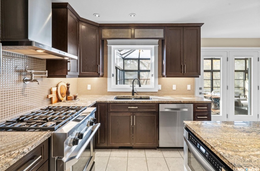 Kitchen with wall chimney range hood, light tile patterned floors, light stone countertops, sink, and stainless steel appliances