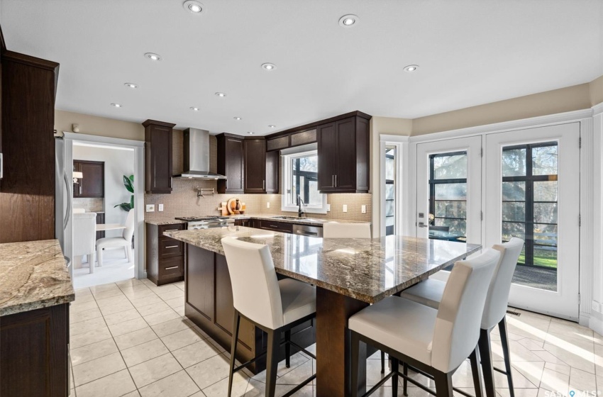 Kitchen featuring wall chimney range hood, a center island, and light stone counters