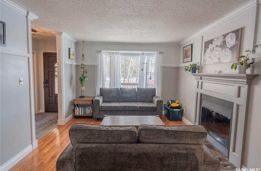 Living area with ornamental molding, a glass covered fireplace, a textured ceiling, light wood-type flooring, and baseboards