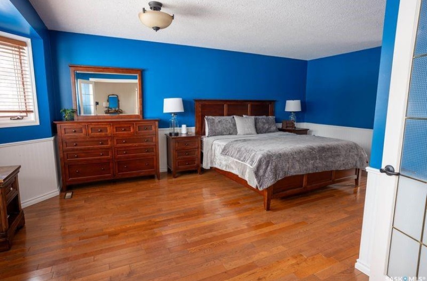 Bedroom with a wainscoted wall, a textured ceiling, and wood finished floors