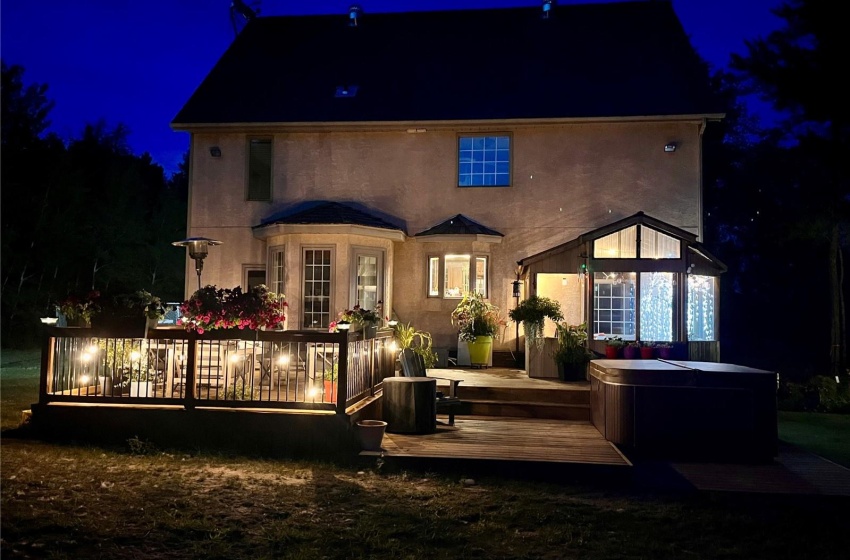 Back of house at night featuring a deck, a covered hot tub, and stucco siding