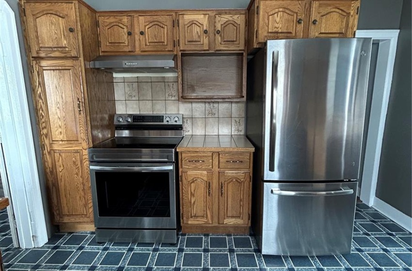 Kitchen with tasteful backsplash, tile counters, range, extractor fan, and fridge