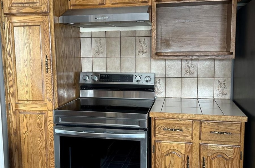 Kitchen featuring tile countertops, extractor fan, refrigerator, electric stove, and brown cabinetry