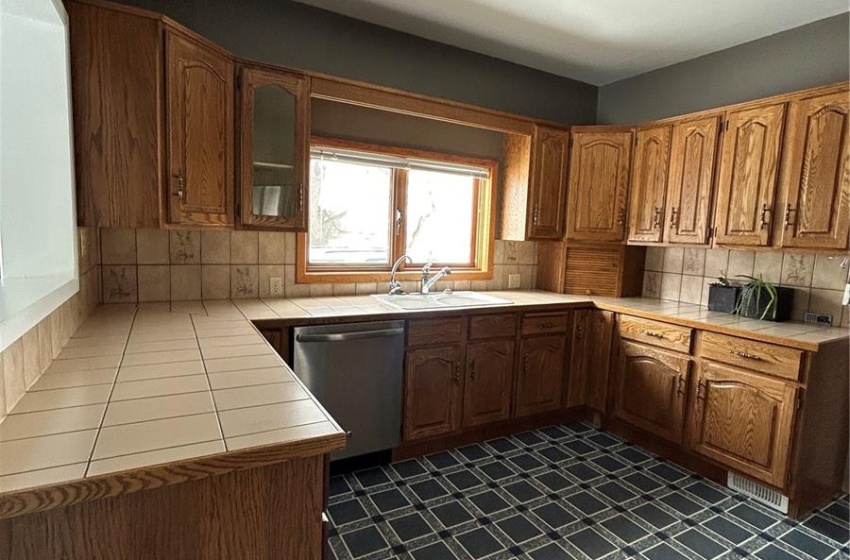 Kitchen featuring tile counters, brown cabinetry, decorative backsplash, dishwasher, and dark floors