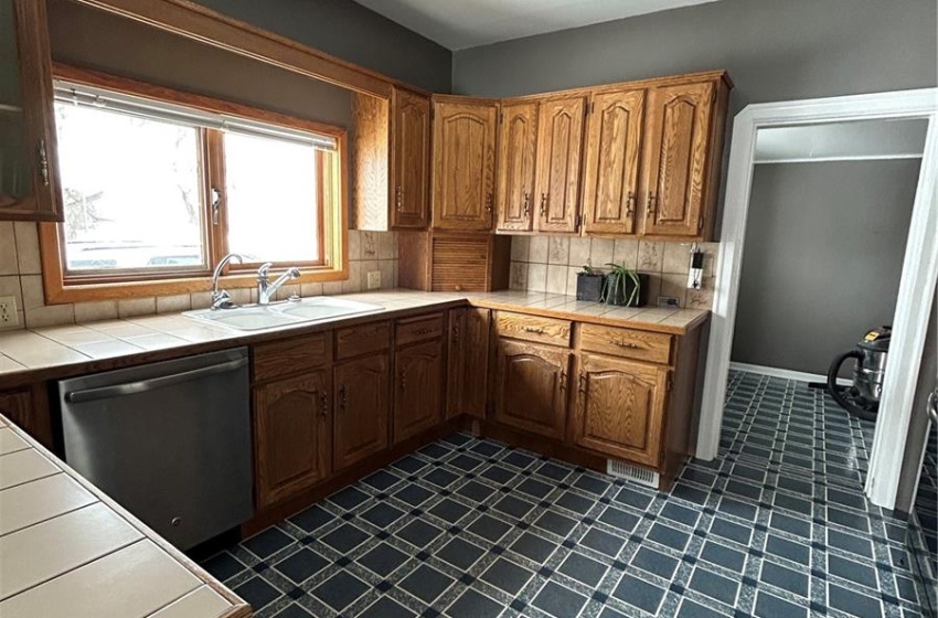 Kitchen featuring tile countertops, dishwashing machine, dark floors, and decorative backsplash