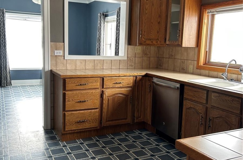 Kitchen featuring dark floors, tasteful backsplash, glass insert cabinets, a sink, and dishwasher