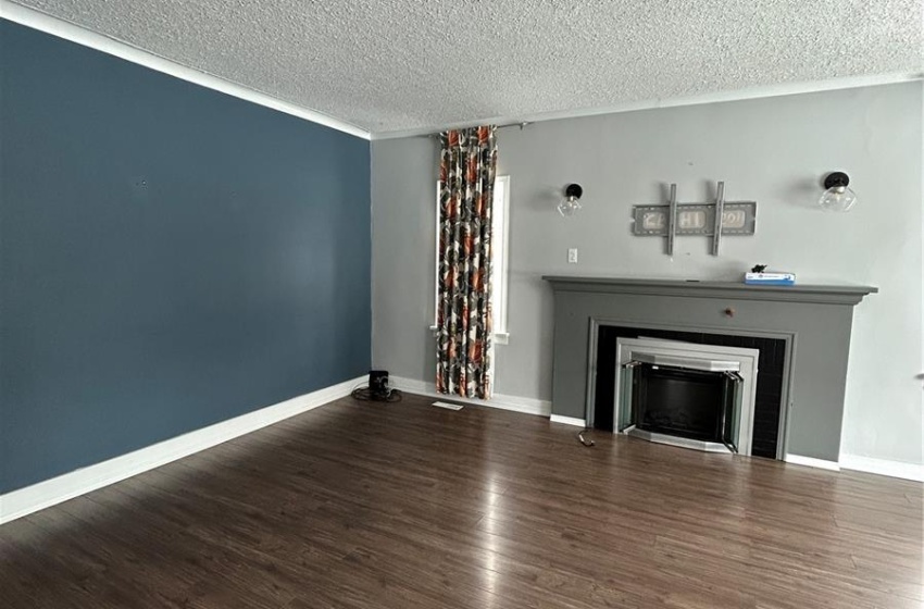 Unfurnished living room with a fireplace, a textured ceiling, baseboards, and wood finished floors