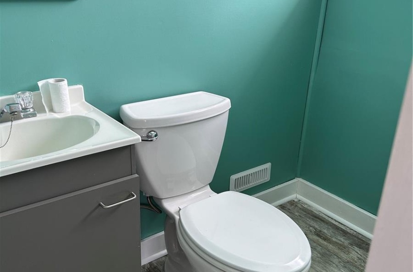 Half bath with toilet, visible vents, wood finished floors, and vanity