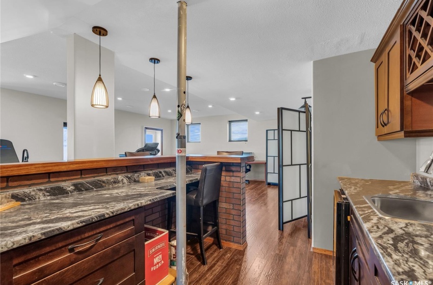 Kitchen featuring dark wood-style flooring, decorative light fixtures, a breakfast bar area, recessed lighting, and a sink
