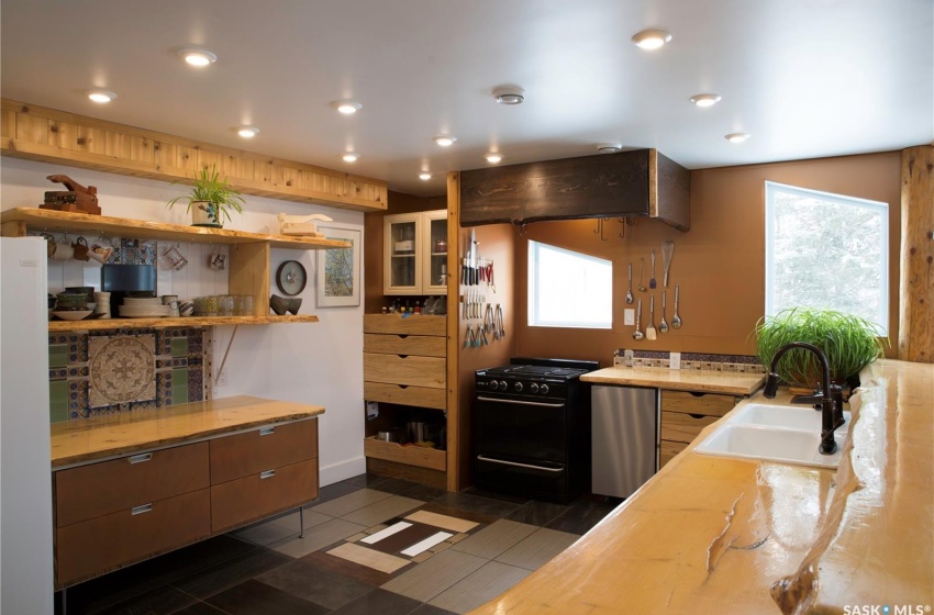 Kitchen featuring island exhaust hood, open shelves, light countertops, black range with gas cooktop, and a sink