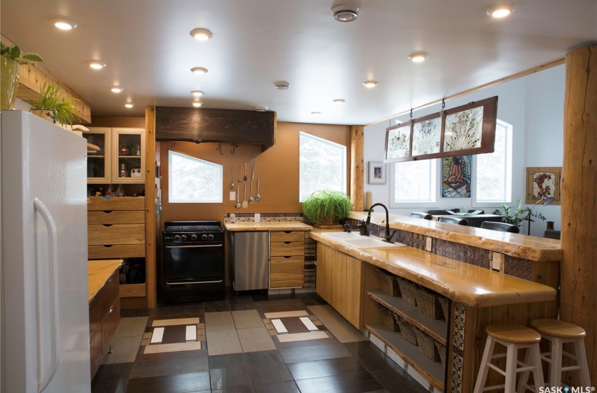 Kitchen featuring a peninsula, a sink, freestanding refrigerator, range hood, and black gas range oven